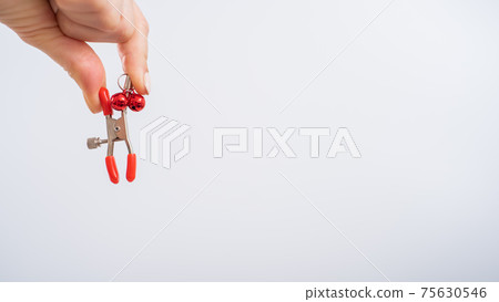 Close up woman's hand holding nipple clamps on a white background. BDSM sex toy 75630546