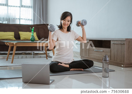 Young girl looking at laptop and doing exercises at home. Young girl looking at laptop and doing exercises at home. 75630688