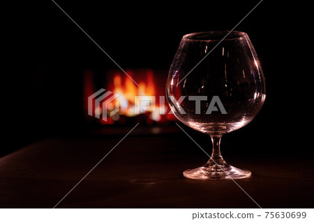 Empty brandy glass on the background of the fireplace in the dark. Empty brandy glass on the background of the fireplace in the dark. 75630699