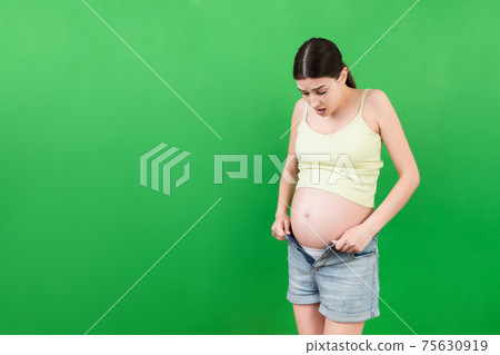 pregnant woman in unzipped jeans showing her naked belly at colorful background with copy space. Baby expecting concept pregnant woman in unzipped jeans showing her naked belly at colorful background with copy space. Baby expecting concept 75630919