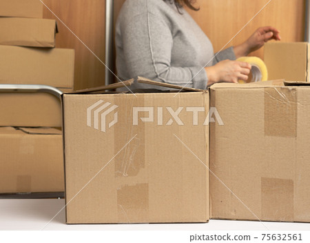 woman in a gray sweater holds a roll of duct tape and packs brown cardboard boxes 75632561
