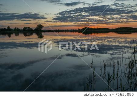 Reflection of clouds in the water of a calm lake after sunset 75633096