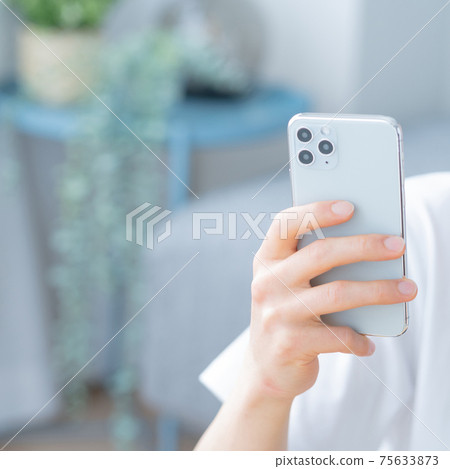Up square at hand of a young man operating a smartphone in the living room Up square at hand of a young man operating a smartphone in the living room 75633873