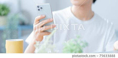 在客廳裡操作智能手機的年輕人的橫幅大小 75633888