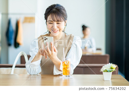 一個年輕的女人，看著一家咖啡館的智能手機 75634202