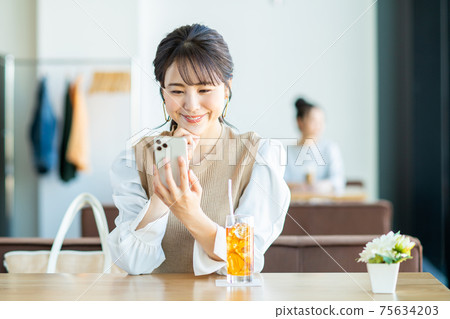一個年輕的女人,看著一家咖啡館的智能手機 一個年輕的女人,看著一家咖啡館的智能手機 75634203