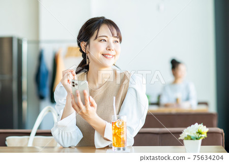 一個年輕的女人,看著一家咖啡館的智能手機 一個年輕的女人,看著一家咖啡館的智能手機 75634204