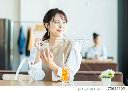 一個年輕的女人,看著一家咖啡館的智能手機 一個年輕的女人,看著一家咖啡館的智能手機 75634205