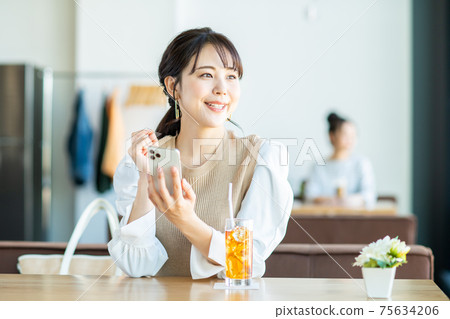 一個年輕的女人,看著一家咖啡館的智能手機 一個年輕的女人,看著一家咖啡館的智能手機 75634206