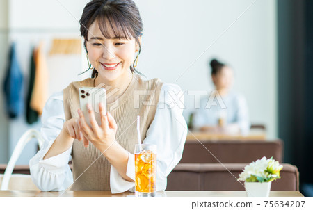 一個年輕的女人,看著一家咖啡館的智能手機 一個年輕的女人,看著一家咖啡館的智能手機 75634207