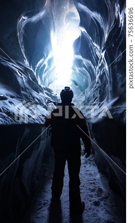 A climber with an ice pick stands at exit of cave 75636696
