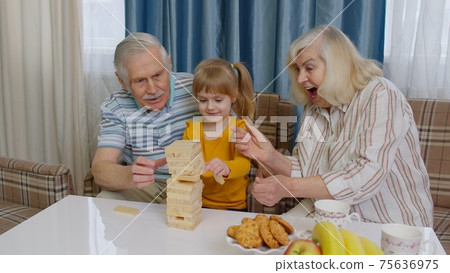 Senior couple grandparents and granddaughter enjoying board game building tower from blocks at home 75636975