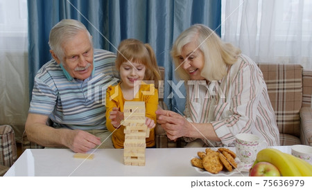 Senior couple grandparents with child kid granddaughter playing game with wooden blocks at home 75636979