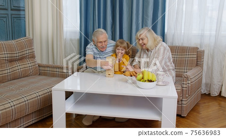 Senior couple grandparents and granddaughter enjoying board game building tower from blocks at home Senior couple grandparents and granddaughter enjoying board game building tower from blocks at home 75636983