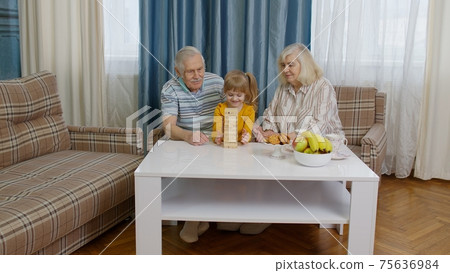 Senior couple grandparents with child kid granddaughter playing game with wooden blocks at home Senior couple grandparents with child kid granddaughter playing game with wooden blocks at home 75636984