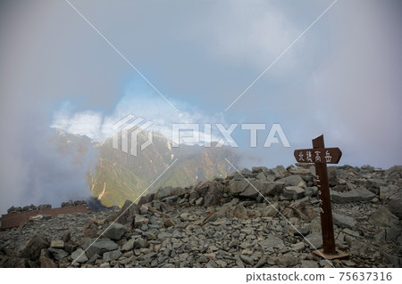 Shinshu Northern Alps Hotaka Mountain Range, Mt. Hotaka Mountain Peak Signpost, Mt. Jonen in the Clouds, Blue Sky. Superb view. Kita-hotaka hut roof on the left 75637316