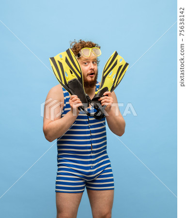 Funny red-headed man in swimming suit and goggles isolated on blue background. Funny red-headed man in swimming suit and goggles isolated on blue background. 75638142