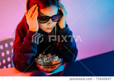 girl in glasses 3D and headphones watches terrible movie on laptop, eats popcorn 75640647
