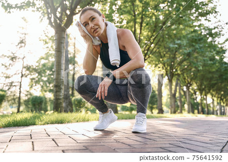 Don't stop. Tired middle aged athletic woman in sportswear wiping her sweat with towel after running in a green park on a sunny day Don't stop. Tired middle aged athletic woman in sportswear wiping her sweat with towel after running in a green park on a sunny day 75641592