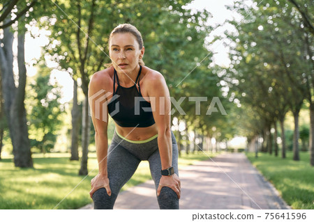 Rest for a while. Beautiful sporty woman in sportswear taking a break while jogging in a green park on a sunny summer day Rest for a while. Beautiful sporty woman in sportswear taking a break while jogging in a green park on a sunny summer day 75641596