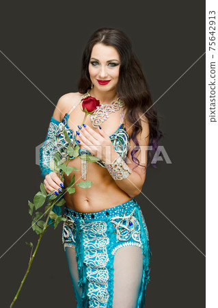 Brunette woman in blue clothes holding a flower near her face 75642913