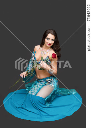 Woman in a blue dress with a rose in her hand sitting on the floor 75642922