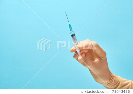 Doctor's hands in gloves hold a syringe with a needle on a blue 75643426