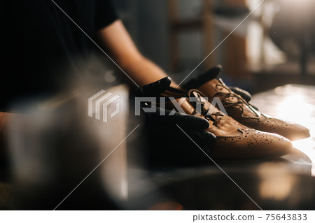 Close-up side view of hands of shoemaker shoemaker in black gloves holding old worn light brown leather shoes Close-up side view of hands of shoemaker shoemaker in black gloves holding old worn light brown leather shoes 75643833