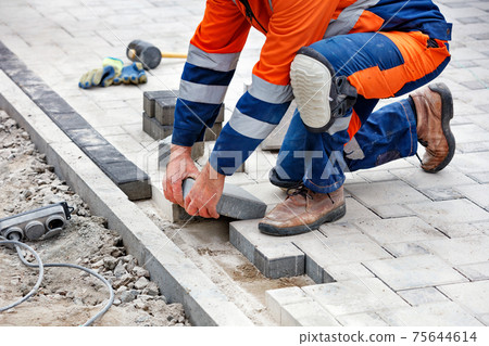 The hands of a working bricklayer are laying paving slabs during the spring day. The hands of a working bricklayer are laying paving slabs during the spring day. 75644614