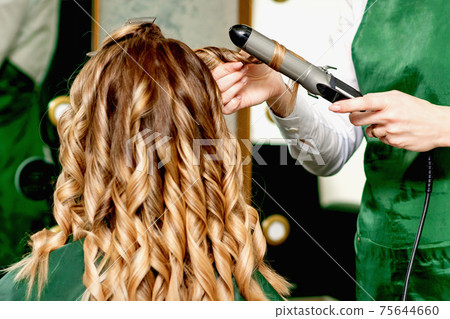 Hairdresser curling hair with curling iron 75644660