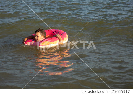 A 5 year old boy swims in the sea, rejoices and has fun in an inflatable ring in the shape of a donut. 75645917