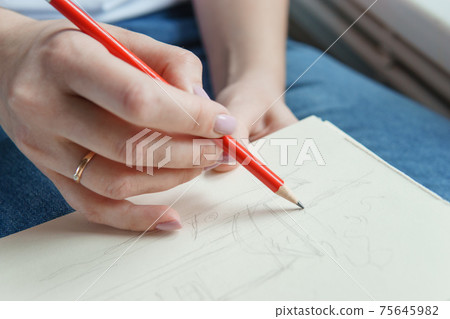 A pencil in a woman's hands. Drawing on a sheet of paper with a simple pencil. The concept of creativity and drawing. A pencil in a woman's hands. Drawing on a sheet of paper with a simple pencil. The concept of creativity and drawing. 75645982
