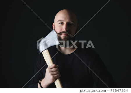 portrait of a man holding an axe near his cheek. photo shoot in the studio on a dark background 75647334