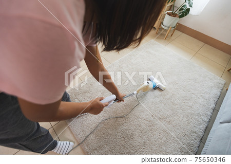 Asian woman cleaning the carpet with vacuum cleaner in the living room. Woman doing chores at home. 75650346