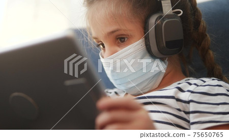 distance learning online lessons. child girl with digital tablet in mask studying remotely at home. education coronavirus online lessons lockdown concept. child learns distance learning school distance learning online lessons. child girl with digital tablet in mask studying remotely at home. education coronavirus online lessons lockdown concept. child learns distance learning school 75650765