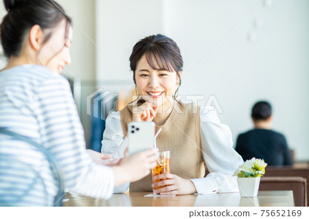 A young woman looking at a smartphone with a friend at a cafe A young woman looking at a smartphone with a friend at a cafe 75652169
