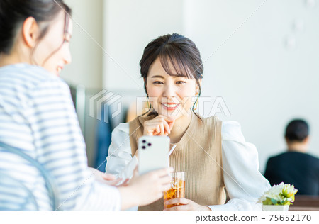 A young woman looking at a smartphone with a friend at a cafe A young woman looking at a smartphone with a friend at a cafe 75652170