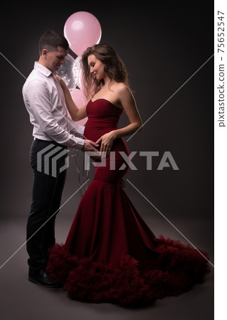Smiling young pregnant couple touching tummy against gray background 75652547