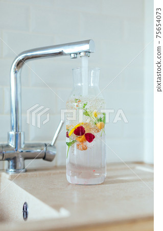 Filling a clear glass carafe with tap water. Water is infused with berries, mint and lemon Filling a clear glass carafe with tap water. Water is infused with berries, mint and lemon 75654073