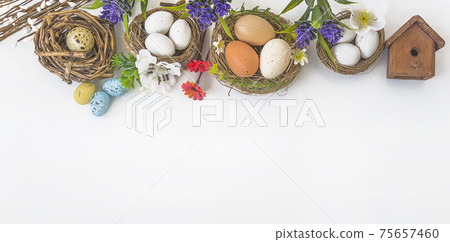 Happy Easter holiday background. Frame of birdnests with eggs, flowers on white background; top view, space for text 75657460