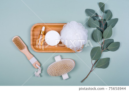 Essential oil or cosmetic serum bottle, massage brushes, face cream on mint background with natural eucalyptus leaves. Beauty products, massage tools, facial skin care, spa beauty treatment concept Essential oil or cosmetic serum bottle, massage brushes, face cream on mint background with natural eucalyptus leaves. Beauty products, massage tools, facial skin care, spa beauty treatment concept 75658944