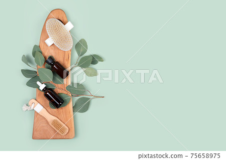 Essential oils and massage brushes with natural eucalyptus leaves on green background. Beauty products, massage tools, facial skin care, spa beauty treatment concept. Flat lay, copy space Essential oils and massage brushes with natural eucalyptus leaves on green background. Beauty products, massage tools, facial skin care, spa beauty treatment concept. Flat lay, copy space 75658975