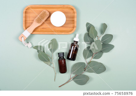 Essential oils, facial creme container and massage brush with natural eucalyptus leaves on green background. Beauty products, massage tools, facial skin care, spa beauty treatment concept. Flat lay Essential oils, facial creme container and massage brush with natural eucalyptus leaves on green background. Beauty products, massage tools, facial skin care, spa beauty treatment concept. Flat lay 75658976