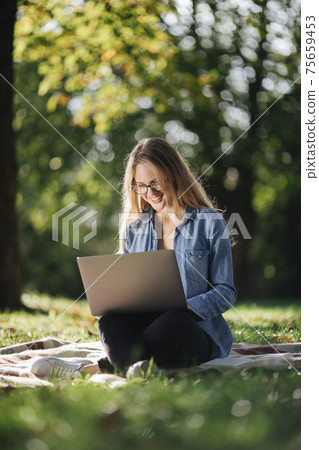 Smiling woman studying on laptop at park 75659453