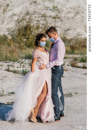 Young loving couple in medical masks in park during quarantine on wedding day. 75659735