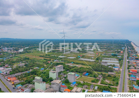 Aerial view of wind turbine with residential buildings in Nakhon Si Thammarat with sea skyline, Thailand. Urban town city in Asia. Architecture landscape background. Aerial view of wind turbine with residential buildings in Nakhon Si Thammarat with sea skyline, Thailand. Urban town city in Asia. Architecture landscape background. 75660414