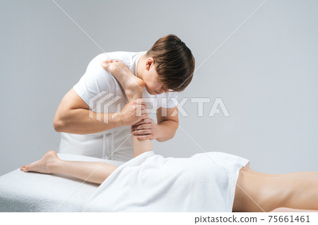 Male masseur with strong hands massaging lower part of leg to young woman on white background 75661461
