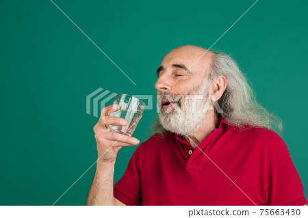Senior grey-haired man with glass of water isolated over green background. Senior grey-haired man with glass of water isolated over green background. 75663430