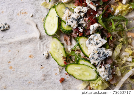 Lavash with vegetables, chicken and cheese on a black background. Lavash with vegetables, chicken and cheese on a black background. 75663717