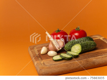 Sliced cucumber, tomatoes and garlic on wooden cutting board. Tomatoes with green ponytails. Healthy food. Copy space. High quality close up photo Sliced cucumber, tomatoes and garlic on wooden cutting board. Tomatoes with green ponytails. Healthy food. Copy space. High quality close up photo 75663835